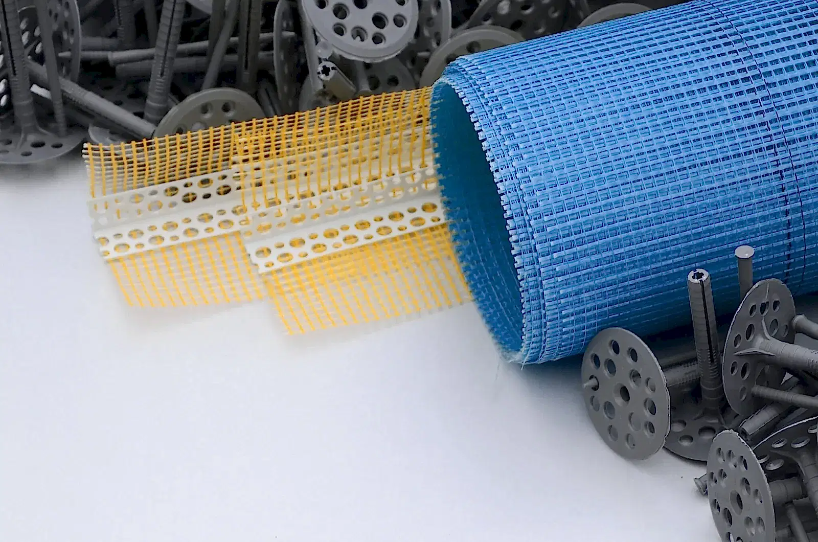 A set of construction items for the insulation of walls. Plastic dowels, a roll of mesh for the insulation of facades and a corner profile with a grid lie on the foam polystyrene surface